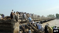Pakistanis use logs and ropes to clamber on a bridge with some of its sections swept away by floodwaters in Charsada, Pakistan on August 1.