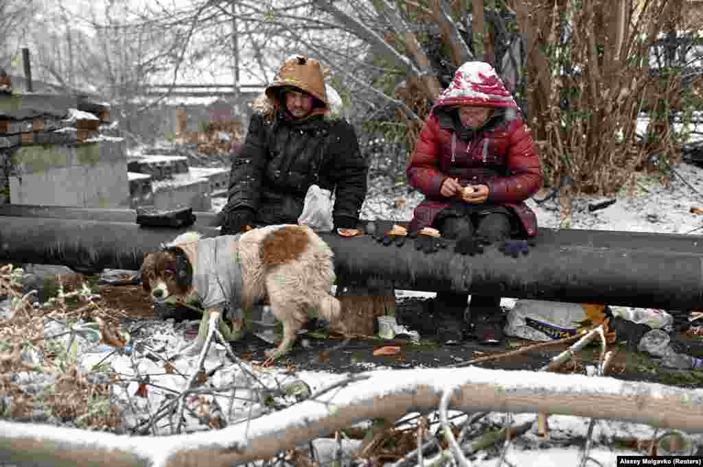 Sasha, 49, nicknamed &quot;Poltorashka&quot; (a 1 1/2-liter beverage bottle), and Lyusya Stepanova, 44, sit on a warm pipe with their dog, Bim, as they share a meal. The pipes provide scalding hot water for heating local buildings.