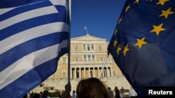 Человек держит флаги Греции и Европейского союза во время митинга у здания парламента в Афинах. 18 июня 2015 года. Иллюстративное фото.