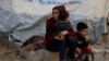 Сирійка з дітьми чекає на отримання допомоги у таборі біженців.