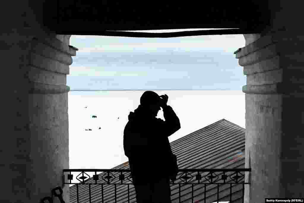 Ivan stands at the bell tower as ice fishermen work in the distance. The people of the monastery have a varied relationship with the fishermen, who occasionally have been accused of property damage or theft. On the other hand, people from the monastery have responded to emergencies for them.