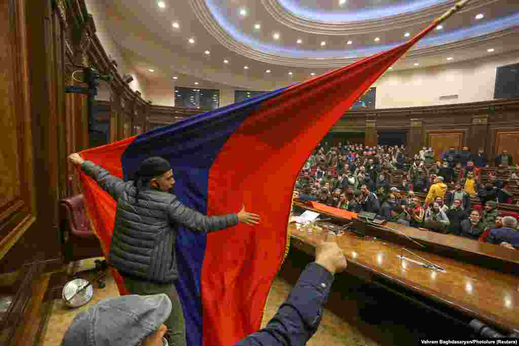 Протестующие вывесили армянский флаг в здании парламента. Они разбрасывали предметы, ломали стулья, а на подиуме вспыхнули потасовки.