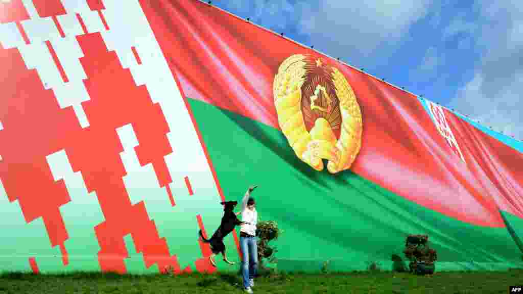 A woman plays with her dog in front of huge images of the Belarusian flag and state emblem in central Minsk on September 24. (AFP/Viktor Drachev)