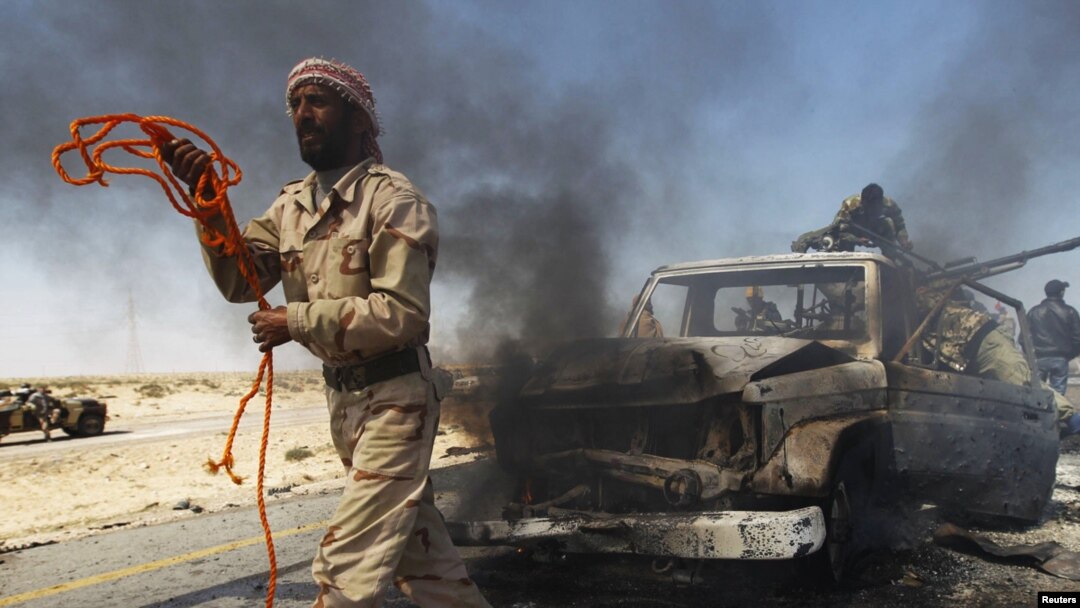 A rebel fighter prepares to tow away a government vehicle mounted with a heavy machine gun after it was hit by a NATO air strike on the eastern outskirts of Brega.