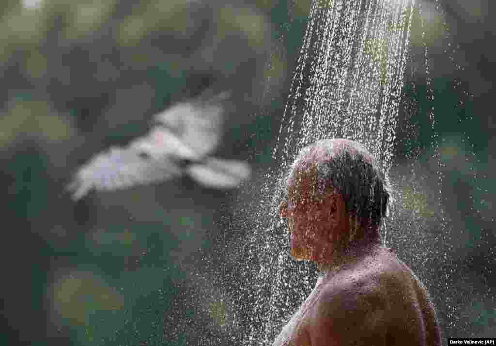 Мужчина принимает холодный душ, чтобы освежиться в жаркую погоду на озере Ада Циганлия в столице Сербии Белграде 14 июля
