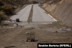 Rruga gjysmë e shtruar ku janë parkuar makineri bujqësore dhe një veturë nga banorët përreth.