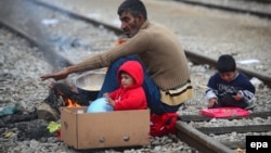 A migrant and his children sit by a fire to warm themselves at the border between Greece and Macedonia near Idomeni on March 17, where up to 40,000 migrants are trapped at the closed crossing.