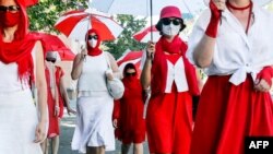 Одетые в белое и красное женщины с зонтами идут по улицам Минска, выражая солидарность с политическими заключенными. 18 июля 2021 года