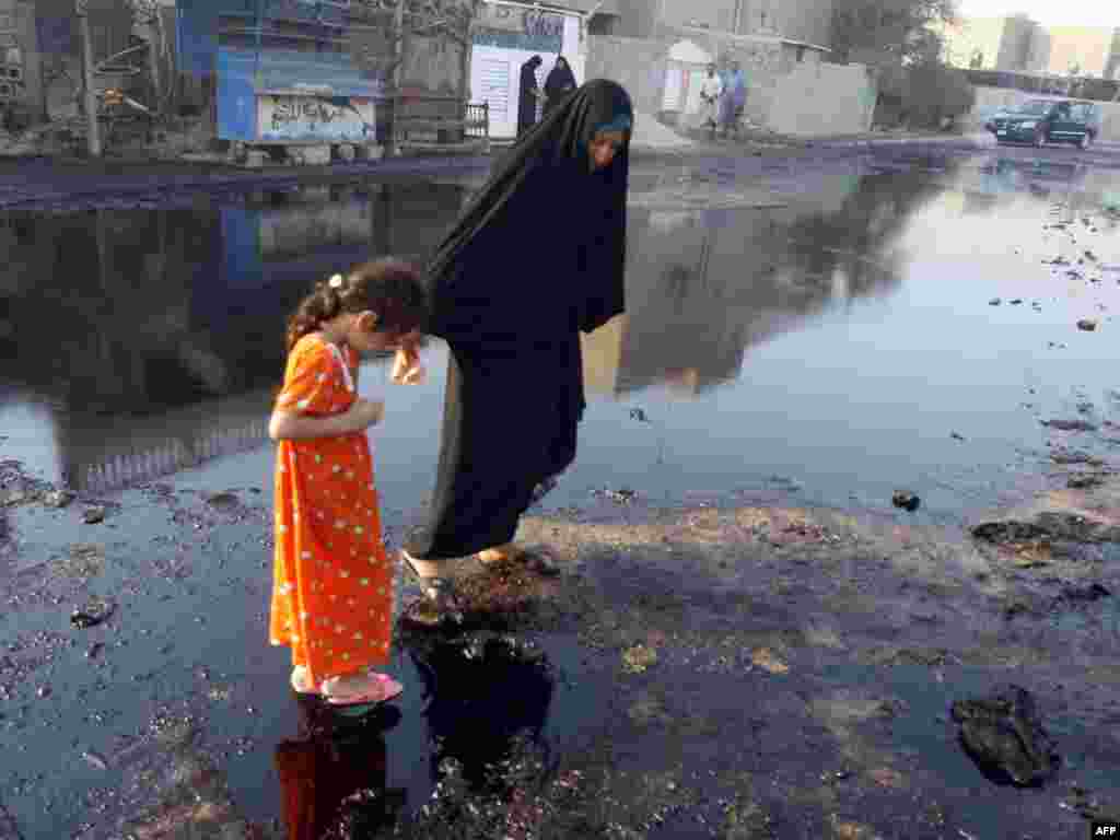 An Iraqi girl is helped by a relative as they walk on spilled oil on August 18 at the spot where a fuel truck exploded in the Iraqi capital's Ur district the previous night, killing two people and injuring more than 20 people.Photo by Ahmad al-Rubaye for AFP