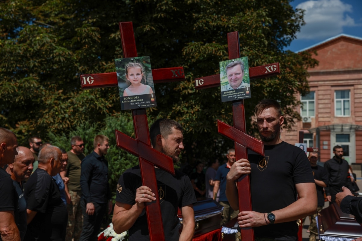 Чоловіки тримають хрести з фотографіями загиблого батька родини Артема Воронова та доньки Емілії. Радушне, Дніпропетровська область, 3 серпня 2026 року.<br><br>3 серпня у Радушному на Дніпропетровщині прощалися з 5 членами сім'ї Воронових, яких вдалося упізнати: батьками родини – подружжям Артемом та Оленою, а також їхніми трьома дітьми: Марком, Азарієм Ілаєм та Емілією