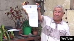 Житель Алматы Зейш Коржинбаев сжигает акт о выселении из дома в Алматы. Скриншот с сайта YouTube. 8 апреля 2014 года.