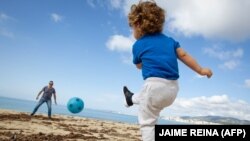 Илустрација: Дете игра фудбал со таткото на плажа во Шпанија