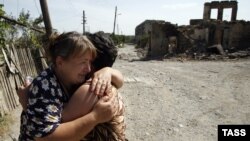 Осетинские женщины обнимают друг друга на фоне руин разрушенного города Цхинвали, столицы непризнанной республики Южная Осетия. Август 2008 года.