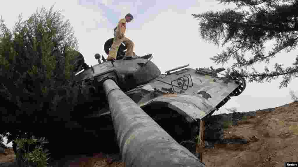 A boy walks on a damaged Syrian Army tank near Idlib on October 2. (REUTERS/Abdalghne Karoof)