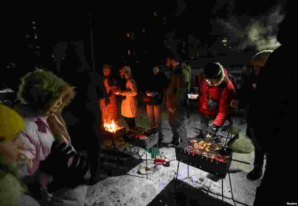 Locuitori ai unui bloc din Kiev gătesc carne la grătar, afară și pe întuneric, în urma deconectării curentului electric ca urmare a atacurilor rusești, pe 18 ianuarie. 