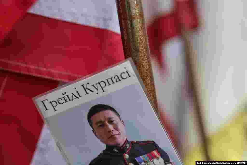Одним із представників першої хвилі був Грейді Курпасі, колишній капітан морської піхоти США та ветеран війни в Іраку. У 2022 році він приєднався до українських сил і служив у розвідувальному підрозділі Інтернаціонального легіону Team Raven. За повідомленнями з відкритих джерел, Курпасі загинув під час бойових дій на Херсонщині, намагаючись врятувати своїх підлеглих від артилерійського обстрілу. Згодом його перепоховали у США на Арлінгтонському національному цвинтарі.На фото: портрет Грейді Курпасі на народному меморіалі пам’яті на майдані Незалежності в Києві, червень 2026 року