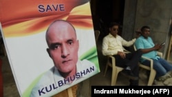 Residents sit next to a placard with a picture of Kulbhushan Sudhir Jadhav, an Indian national convicted of spying in Pakistan, in the neighborhood where he grew up, in Mumbai on July 17.