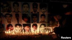 A man places a rose after lighting candles in front of portraits of the victims of the Taliban attack on the Army Public School in Peshawar, during a candlelight vigil in Lahore in this December 19, 2014 file photo.