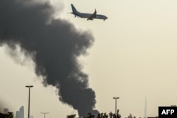 Cамолет авиакомпании FlyDubai готовится к посадке в международном аэропорту Дубая на фоне поднимающегося столба дыма от продолжающегося там поблизости пожара, вызванного ударом иранского дрона. 16 марта 2026 года