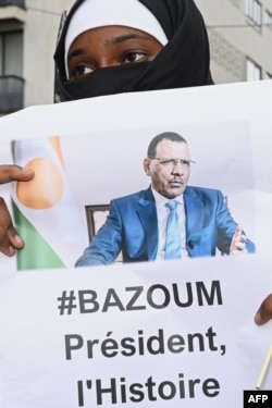 Женщина держит изображение свергнутого президента Нигера Мохамеда Базума во время акции протеста у посольства Нигерии в Париже 5 августа
