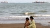 Iranian women walk along the seashore as vessels are seen in the Strait of Hormuz off the port city of Bandar Abbas in southern Iran . 