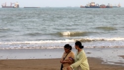 Iranian women walk along the seashore as vessels are seen in the Strait of Hormuz off the port city of Bandar Abbas in southern Iran . 