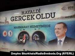 «Мрії збуваються. Мармаріє до ваших послуг». Мармаріє («Залізниця Мармурового моря») – гілка стамбульського метрополітену, що перетинає протоку Босфор. Довжина тунелю, який пролягає під дном протоки, становить 1.4 кілометра. Рекламний банер президента Туреччини Реджепа Ердогана, який у роки будівництва гілки метро очолював уряд країни.