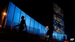 Pedestrians walk by United Nations Headquarters, lit up in blue light, a day in advance of the 70th Anniversary of the U.N., Friday, Oct. 23, 2015, in New York. Around 200 other buildings and structures in 60 other countries were also lit in blue to comme