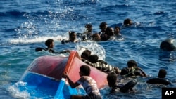 Migránsok úsznak felborult facsónakjuk mellett az olaszországi Lampedusa sziget közelében 2022. augusztus 11-én