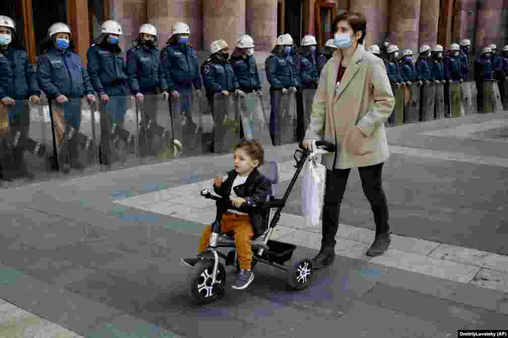 A woman wheels a stroller with a child as police officers guard the government building in Yerevan on November 10. Thousands of people streamed into the main square in the Armenian capital on November 10 to protest an agreement to halt fighting over the breakaway Nagorno-Karabakh region, many shouting, &quot;We won&#39;t give up our land!&quot; (AP/Dmitri Lovetsky)