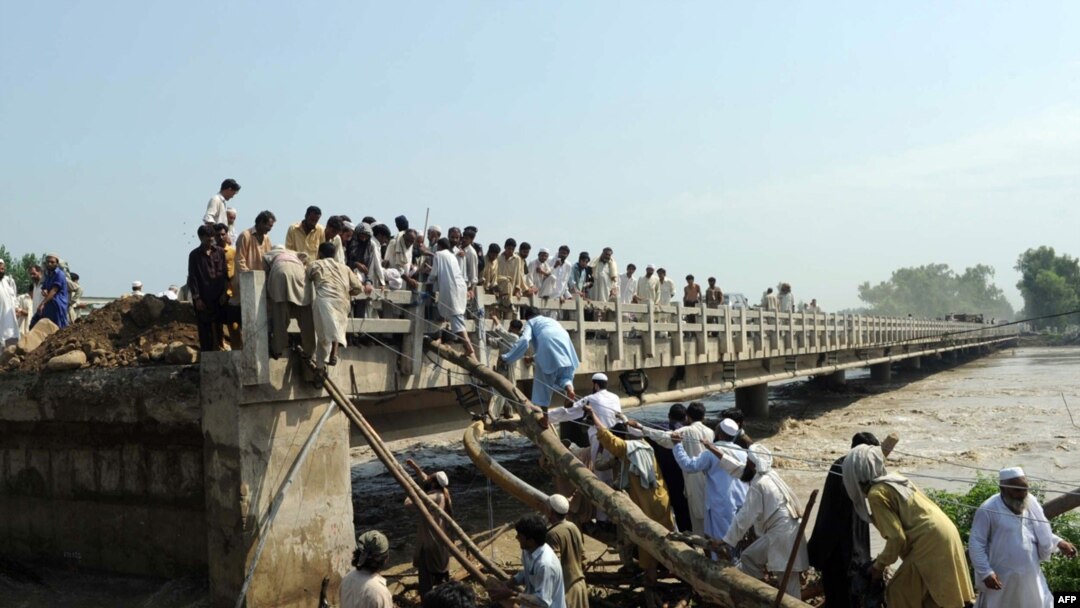 Pakistanis use logs and ropes to clamber on a bridge with some of its sections swept away by floodwaters in Charsada, Pakistan on August 1.
