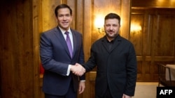 Украинанын президенти Владимир Зеленский (оңдо) 62-Мүнхен коопсуздук жыйынында АКШнын мамлекеттик катчысы Марко Рубио (солдо) менен кол алышып жаткан учур. 14-февраль, 2026-жыл. 