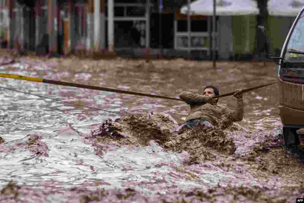 A man clings to a security line to cross a street flooded by the overflowing Copiapo River due to heavy rainfall that affected some areas in the city in Chile on March 26. (AFP)