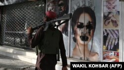 Боевик «Талибана» проходит мимо уже бывшего салона красоты с изображениями женщин, испачканными аэрозольной краской. Кабул, 18 августа 2021 года