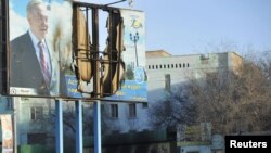 Kazakhstan -- Interior Ministry troops patrol beneath a poster of President Nursultan Nazarbaev and partially burnt buildings damaged in recent riots in the town of Zhanaozen, 19Dec2011