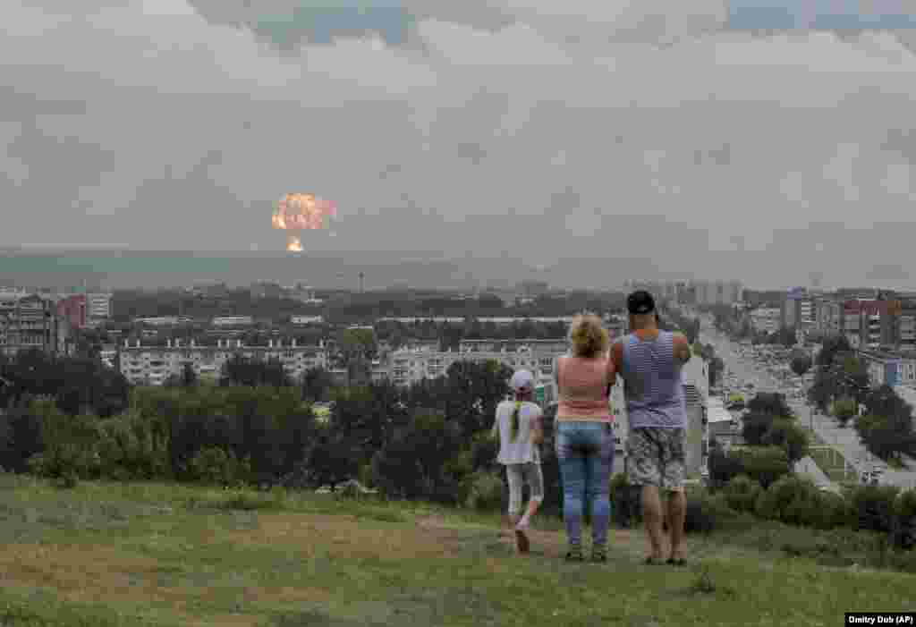 A family watches explosions at a military ammunition depot near the city of Achinsk in eastern Siberia&#39;s Krasnoyarsk region, on August 5. The powerful explosions left at least 12 people injured and one missing and forced around 15,000 people to leave their homes. (AP/Dmitry Dub)