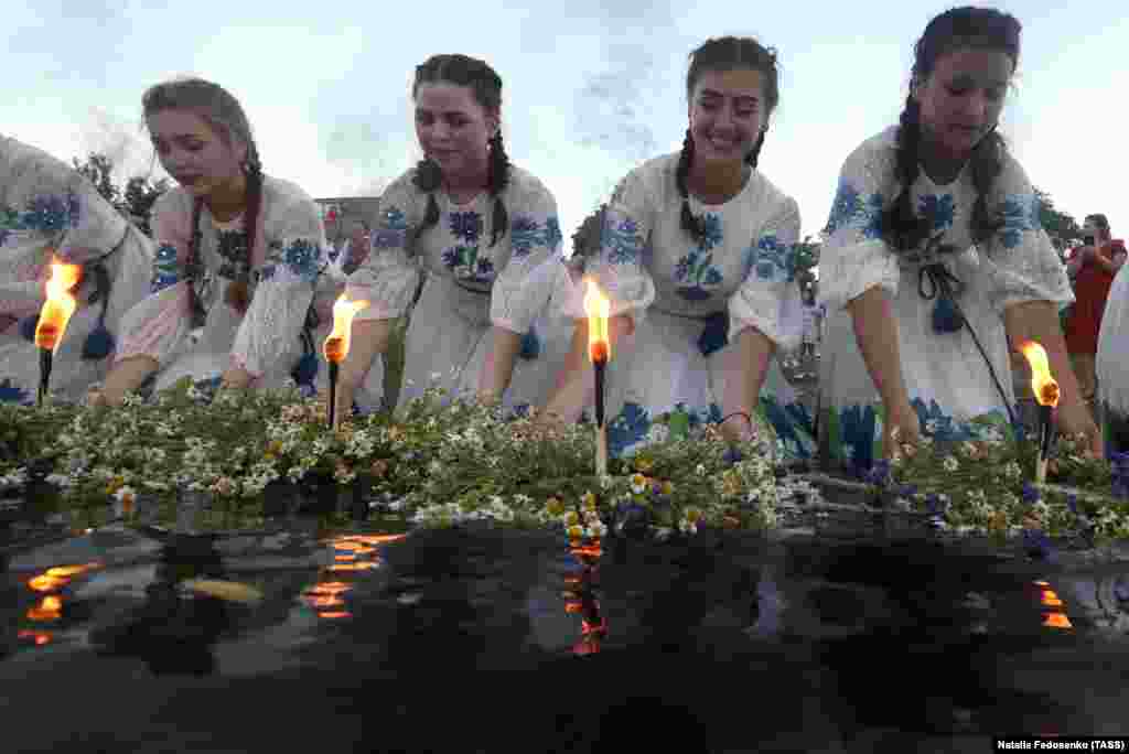 Girls in ethnic costumes light candles on flower wreaths by the Pripyat River.