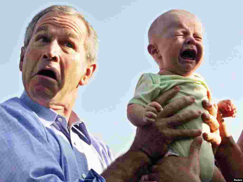 U.S. President George W. Bush hands back a crying baby that was handed to him from the crowd as he arrived for an outdoor dinner with German Chancellor Angela Merkel in Trinwillershagen, Germany, July 13, 2006. REUTERS/Jim Bourg 