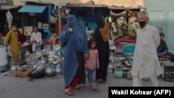 A burqa-clad Afghan woman looks for items to buy at a shop displaying used household items for sale at a market area in Kabul.