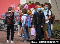 Egy csapat gyerek maszkban virágot visz a tanárának egy bukaresti iskolában 2020. szeptember 14-én.