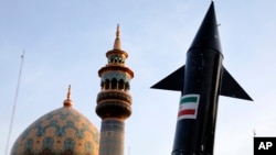 Иранските демонстранти носат модел на проектил додека во позадина се гледаат минарето и куполата на џамијата за време на антиизраелскиот митинг во Техеран, 15 април 2024 година