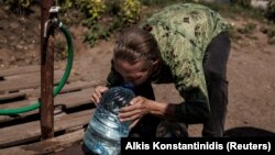 Egy nő tiszta vizet iszik az éppen feltöltött kannából a keleti Szlovjanszk városában