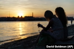 Tanya Lavzinenko (right) and a friend sit on a beach with glasses of prosecco while watching the sun set over the Dnieper River in Kyiv on July 31.