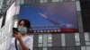 زنی از کنار تلویزیونی که رزمایش نظامی چین در آبراه تایوان را نشان می‌دهد عبور می‌کند