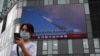 Žena koristi mobilni telefon dok hoda ispred velikog ekrana na kojem se prikazuju vijesti o kineskim vojnim vježbama koje okružuju Tajvan, u Pekingu 4. avgusta 2022.