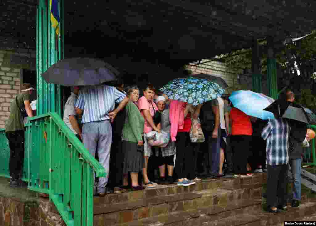 Жителите чекаат да земат торби со храна во малото село Малаја Рохан на 4 август. Селото, кое се наоѓа источно од Харкив, беше тешко оштетено откако претрпе неколку недели руско гранатирање и окупација. &nbsp;