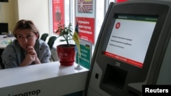 An employee sits next to a payment terminal out of order at a branch of Ukraine's state-owned Oschadbank in Kyiv on June 27.