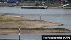 Egy uszály halad a Rajnán, miközben az előtérben a részben kiszáradt folyómeder látható a németországi Düsseldorfban 2022. július 25-én