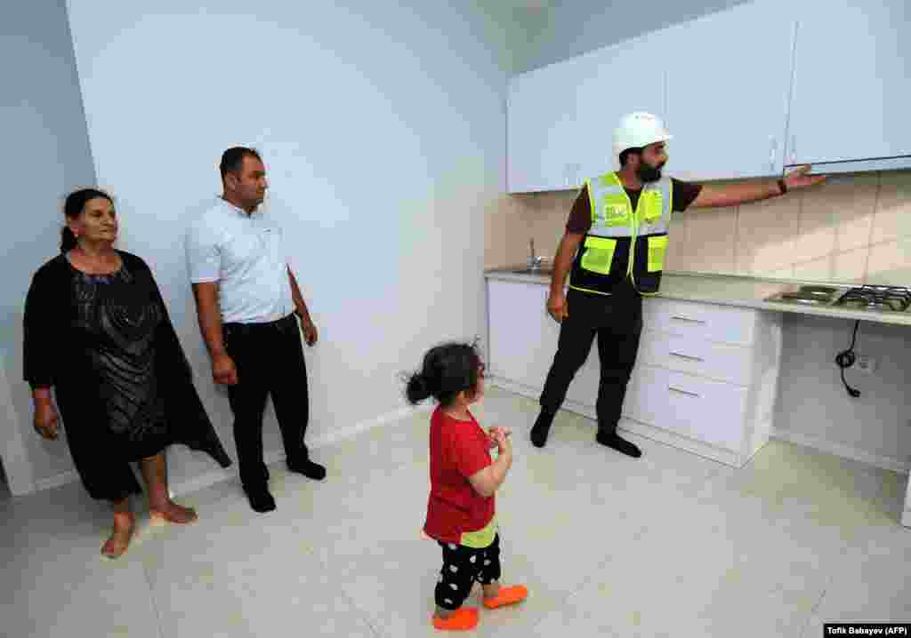 A family are shown around houses in Agali on July 19. Azerbaijanis who were displaced by the 1988-1994 Nagorno-Karabakh war have reportedly been offered to have the cost of moving into recaptured territories paid for by the state.