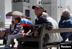 Мужчина с российским флагом сидит перед зданием Мариупольского театра, разрушенным в ходе российской бомбардировки. Мариуполь, 30 мая 2022 года